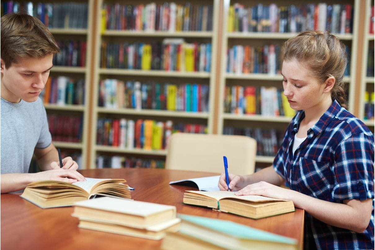 Two students studying together at a table, surrounded by books.